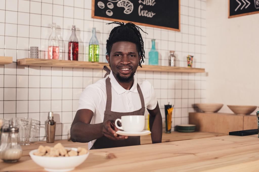 souriant afro-américaine barista dans tablier donnant tasse de café
  - Photo, image