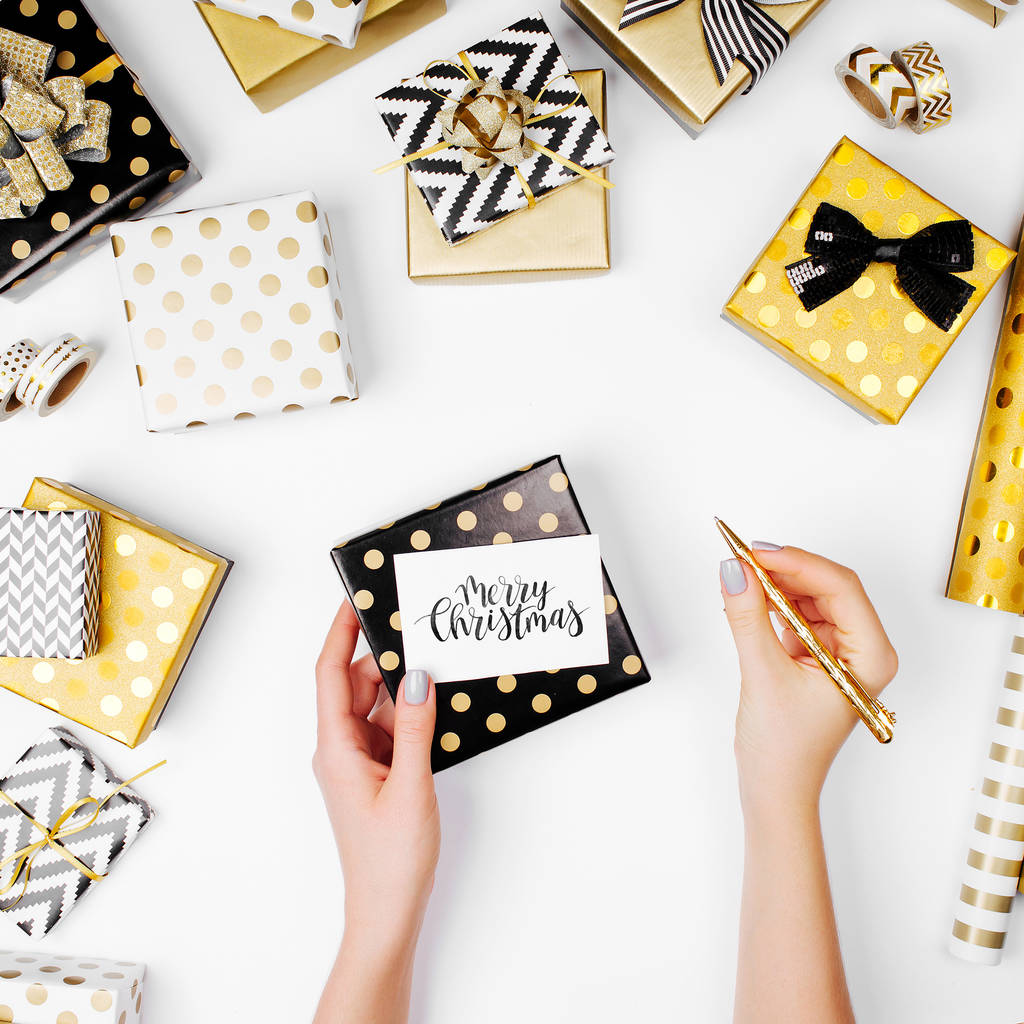 manos femeninas sosteniendo la tarjeta de felicitación de Feliz Navidad. Colocación plana de regalos dorados y papel de regalo sobre fondo
  - Foto, imagen