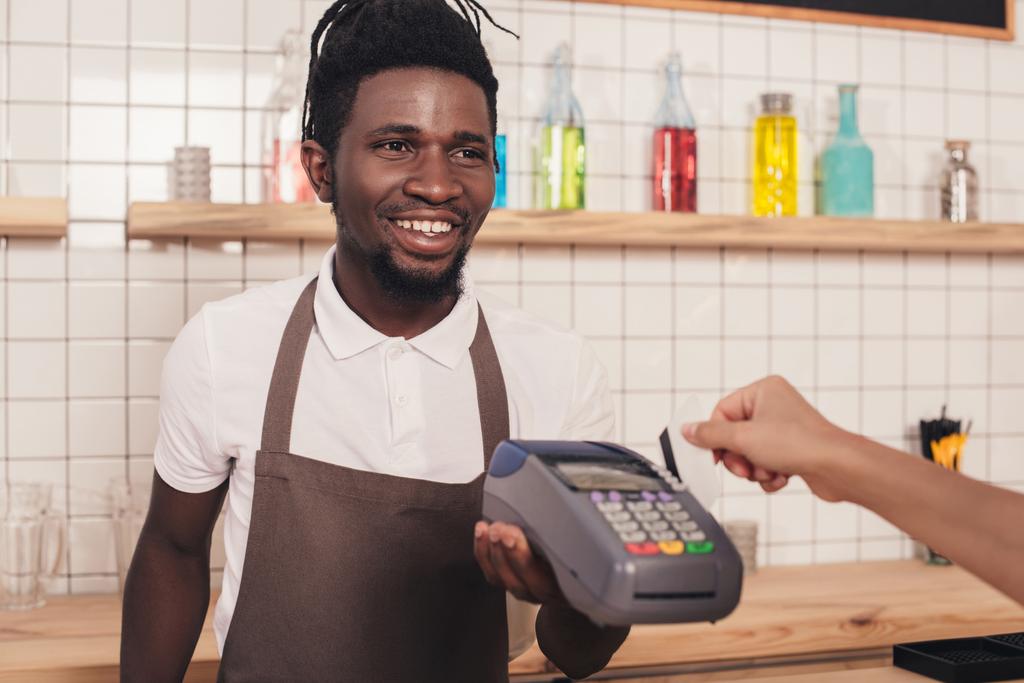 Barista holding terminal terwijl client betalen met credit card in café - Foto, afbeelding
