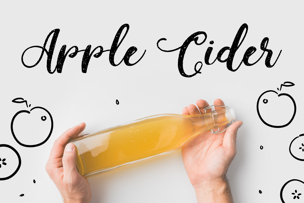top view of person holding bottle of cider with hand drawn apples and lettering on white surface - Photo, Image
