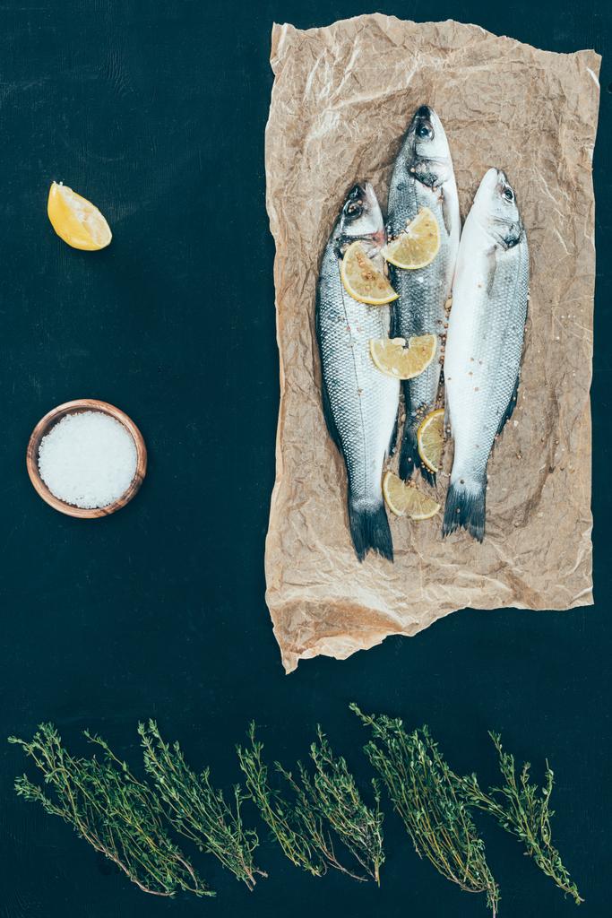 верхний вид здоровой рыбы с ломтиками лимона на бумаге на черном
 - Фото, изображение