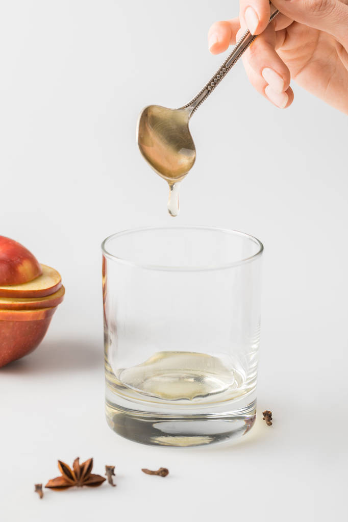 oříznutý snímek žena vylévající medu ve sklenici od lžíce na bílém stole - Fotografie, Obrázek
