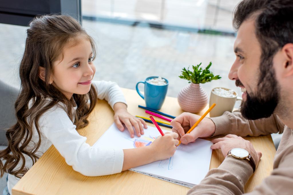smiling daughter and father drawing together and looking at each other - Photo, Image