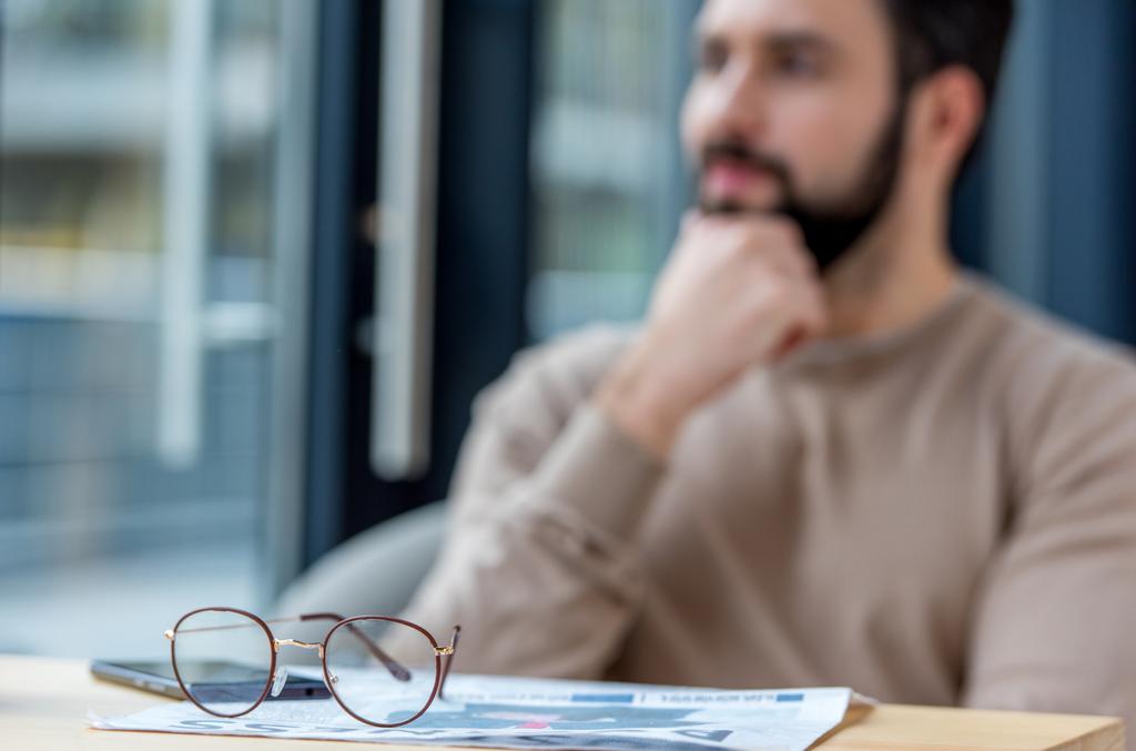 Nachdenklicher Mann sitzt im Café mit Brille im Vordergrund - Foto, Bild