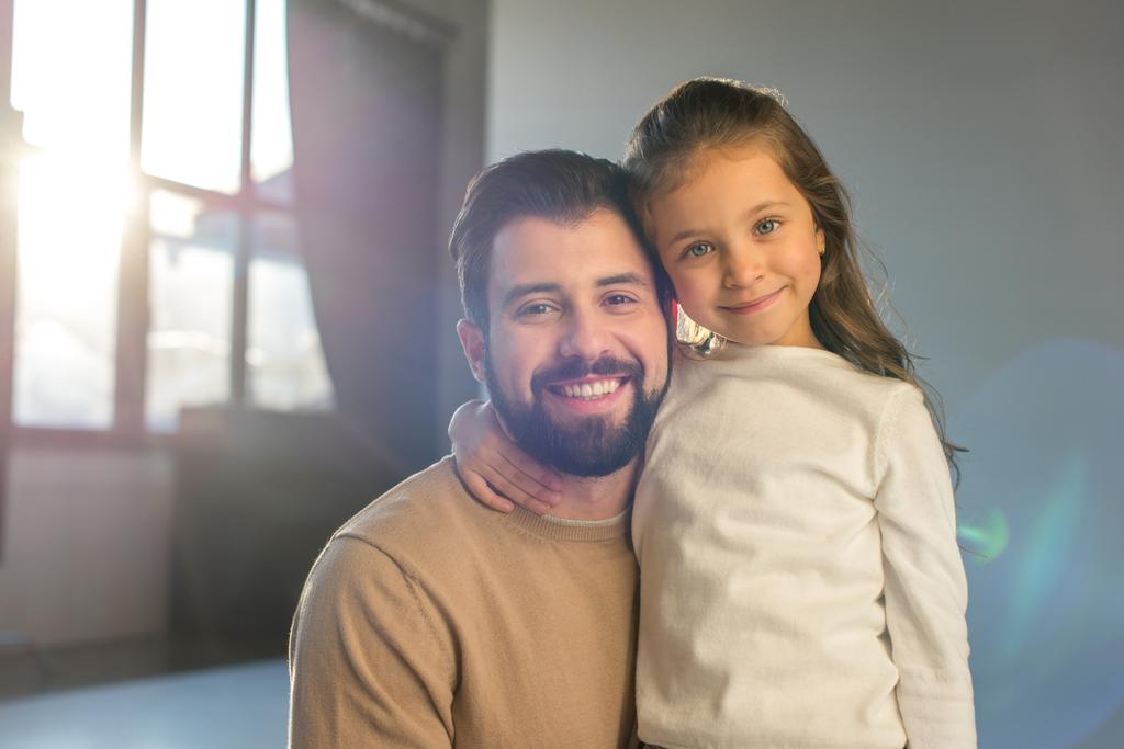smiling father and daughter posing in room and looking at camera - Photo, Image