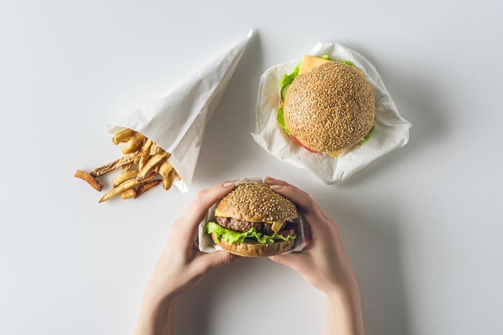 vue recadrée des mains avec hamburgers et frites en cône de papier, isolé sur blanc
 - Photo, image
