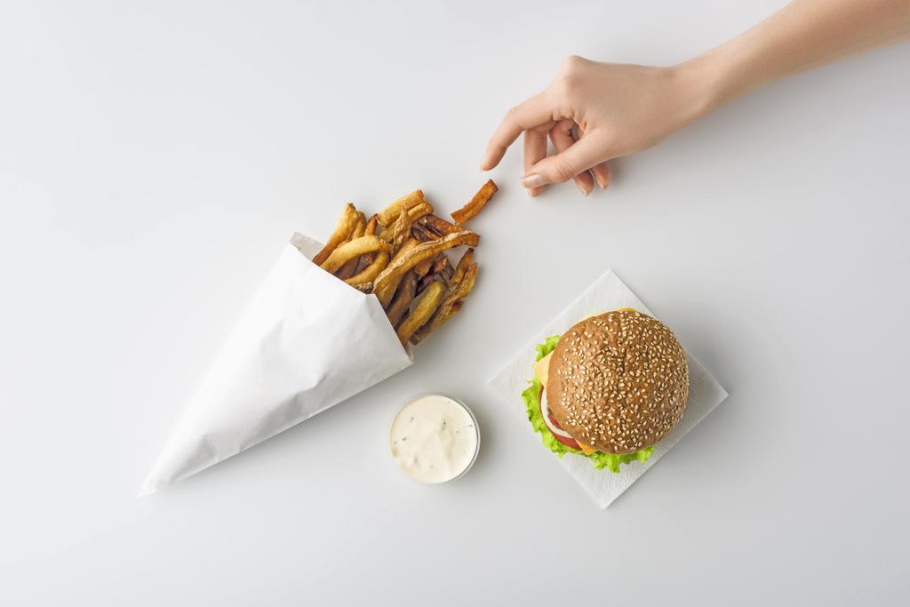 vista recortada de la mano femenina con papas fritas, hamburguesa casera y mayonesa, aislado en blanco
 - Foto, Imagen
