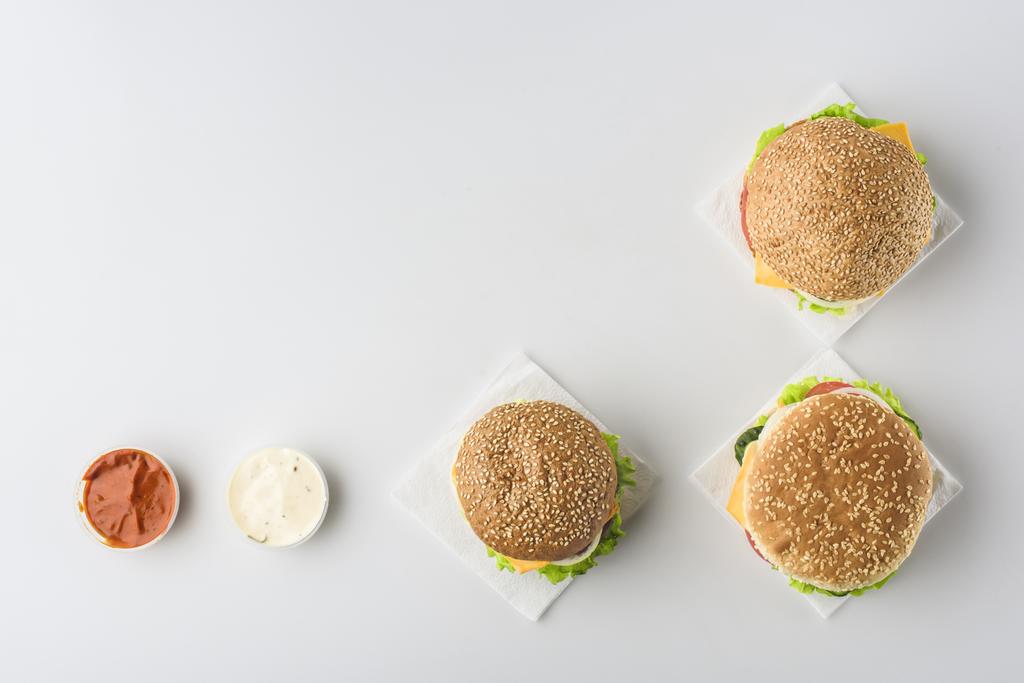 вид сверху на соусы и гамбургеры на салфетках, изолированные на белом
 - Фото, изображение