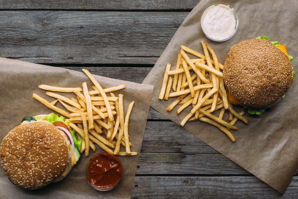 Draufsicht auf Hamburger, Pommes und Soßen auf Backpapier auf Holztischplatte - Foto, Bild