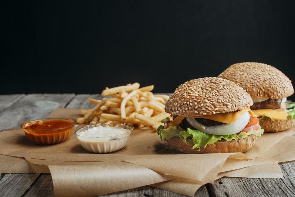 traditionelle hausgemachte Cheeseburger auf Backpapier mit Pommes frites, Ketchup und Mayonnaise-Saucen - Foto, Bild