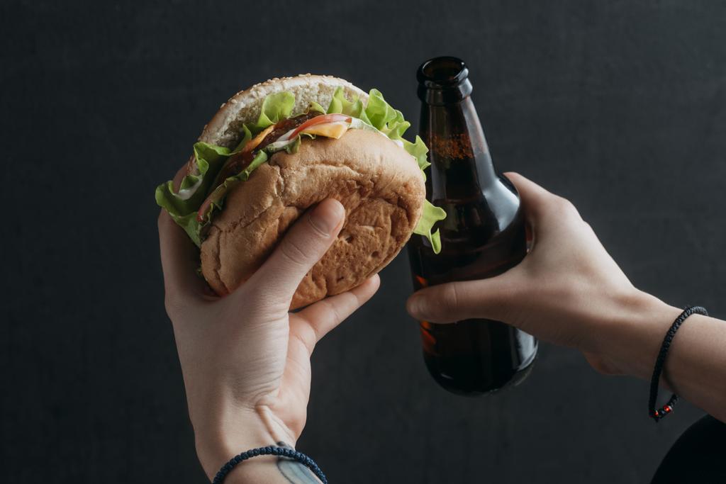 hamburger ve bira şişe tutan kişinin görünümü kırpılmış - Fotoğraf, Görsel