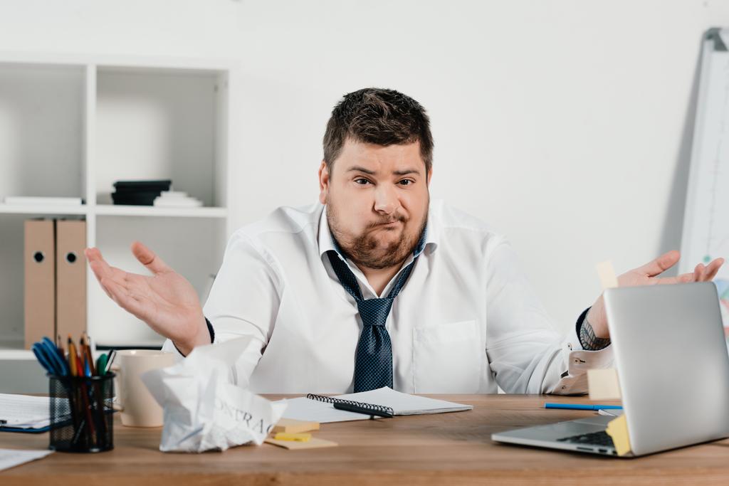 zavaros túlsúlyos üzletember ül a munkaterület, iratok és laptop  - Fotó, kép