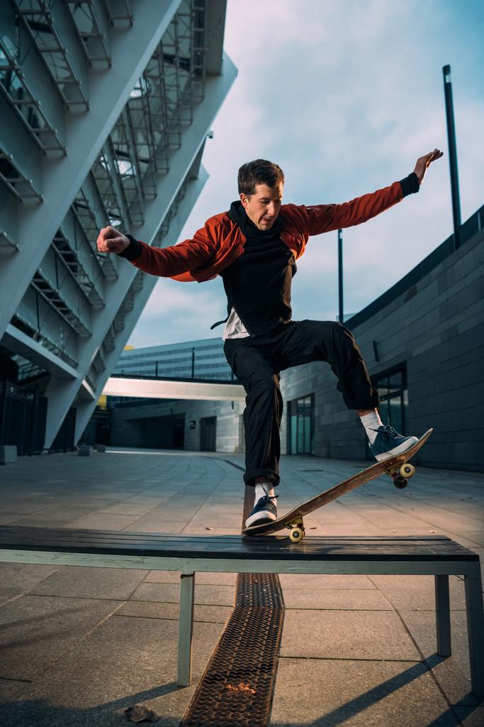 Junge Skateboarderin balanciert im schicken Outfit mit Brett auf Bank - Foto, Bild