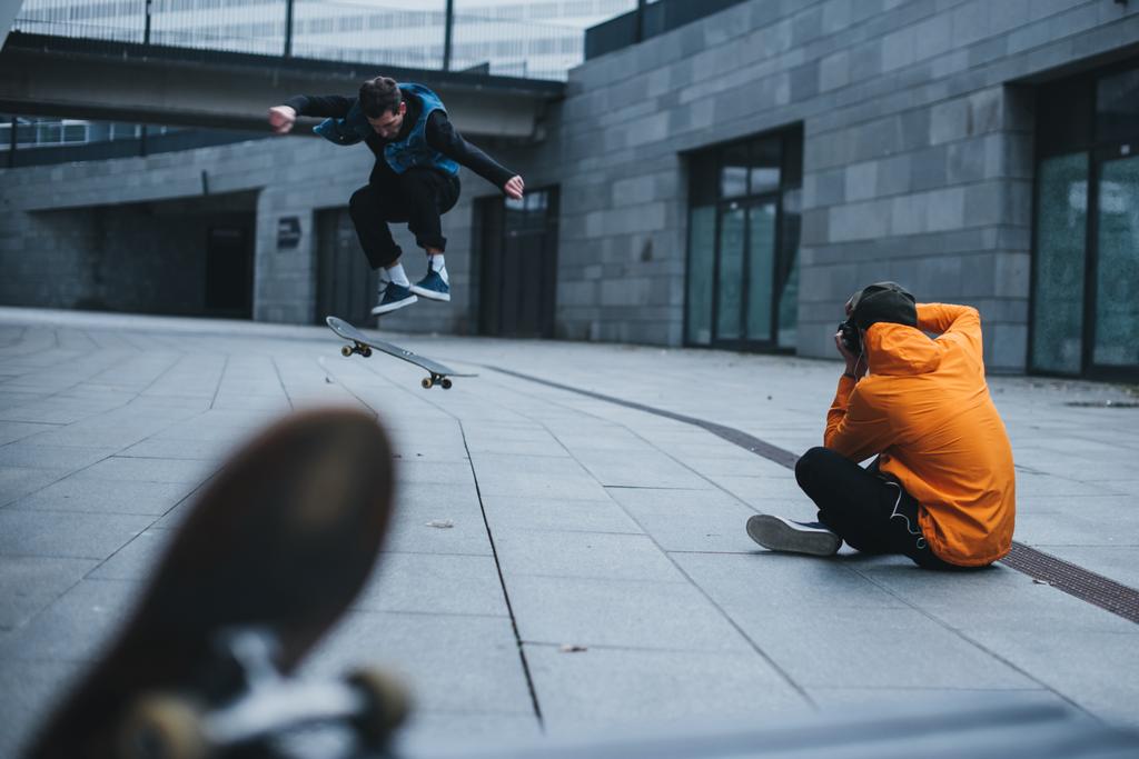 homem sentado no chão e tirar fotos de skatista fazendo truque
 - Foto, Imagem