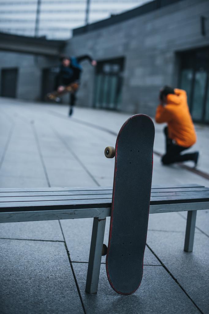 Скейтбордисты фотографируют трюки со скейтбордом, опирающимся на скамейку на переднем плане
 - Фото, изображение
