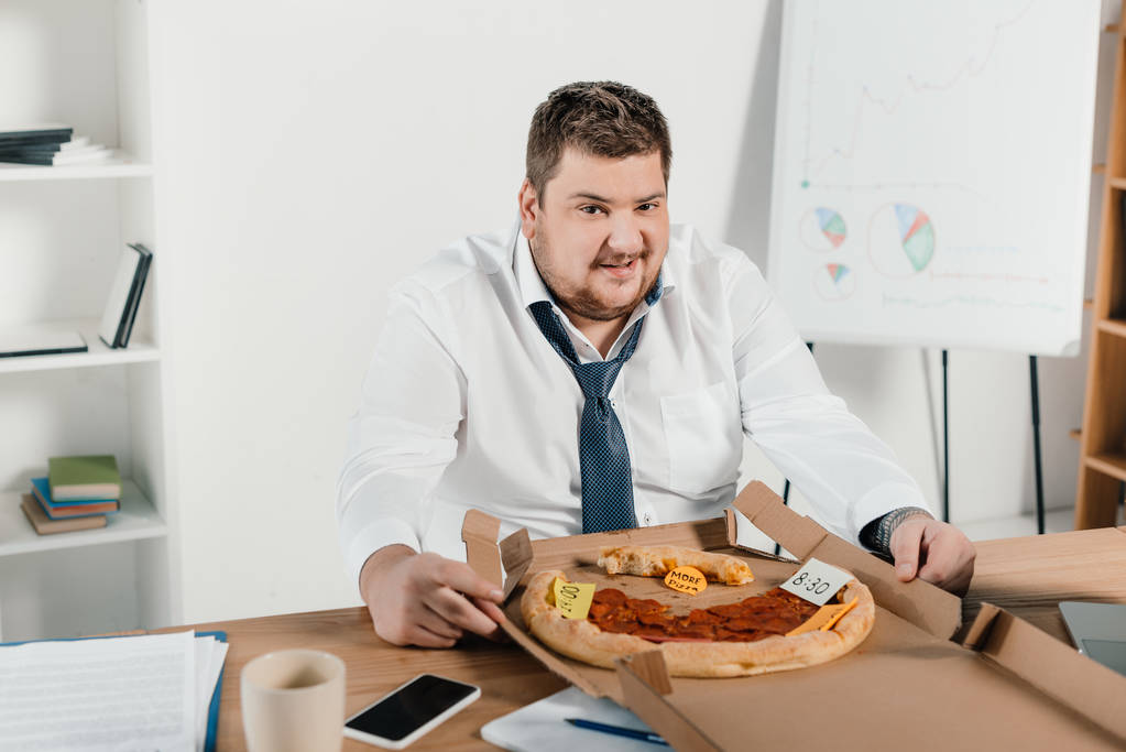 empresário com excesso de peso comer pizza no local de trabalho no escritório
 - Foto, Imagem