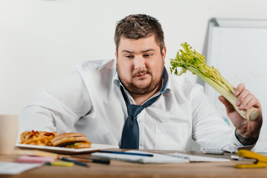 nachdenklicher übergewichtiger Geschäftsmann, der sich am Arbeitsplatz im Büro für gesundes oder Junk Food entscheidet - Foto, Bild