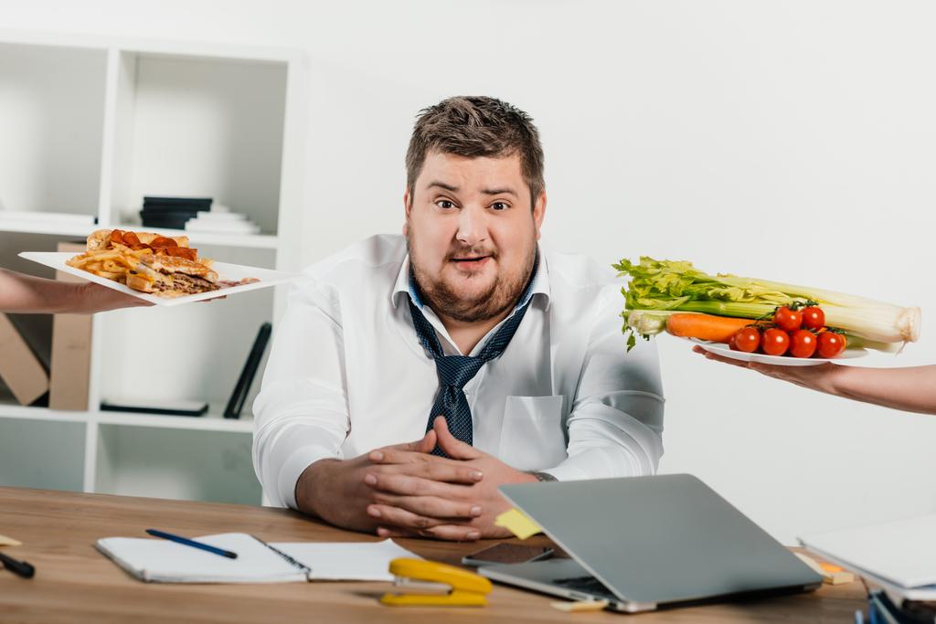 υπέρβαροι επιχειρηματίας επιλέγοντας υγιεινά ή πρόχειρο φαγητό στο χώρο εργασίας στο γραφείο - Φωτογραφία, εικόνα