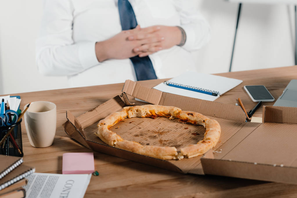 vista cortada de empresário gordo comer pizza no local de trabalho
  - Foto, Imagem