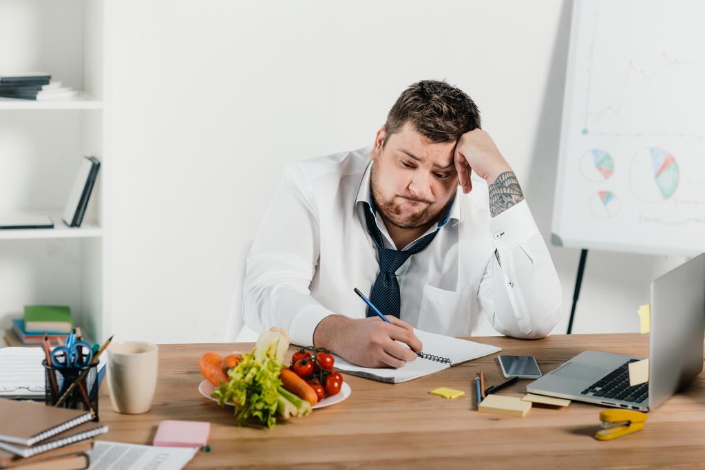 расстроен лишний вес бизнесмен смотрит на овощи во время работы в офисе
 - Фото, изображение