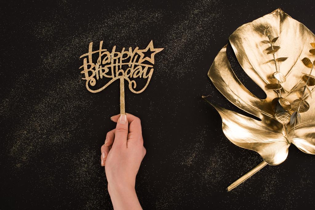 обрезанный снимок женской руки с счастливым знаком дня рождения с золотым листом, лежащим рядом
 - Фото, изображение