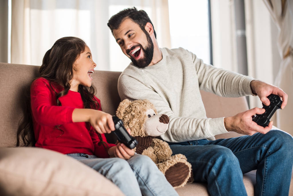 pai feliz e filha jogando videogame em casa e olhando um para o outro
 - Foto, Imagem