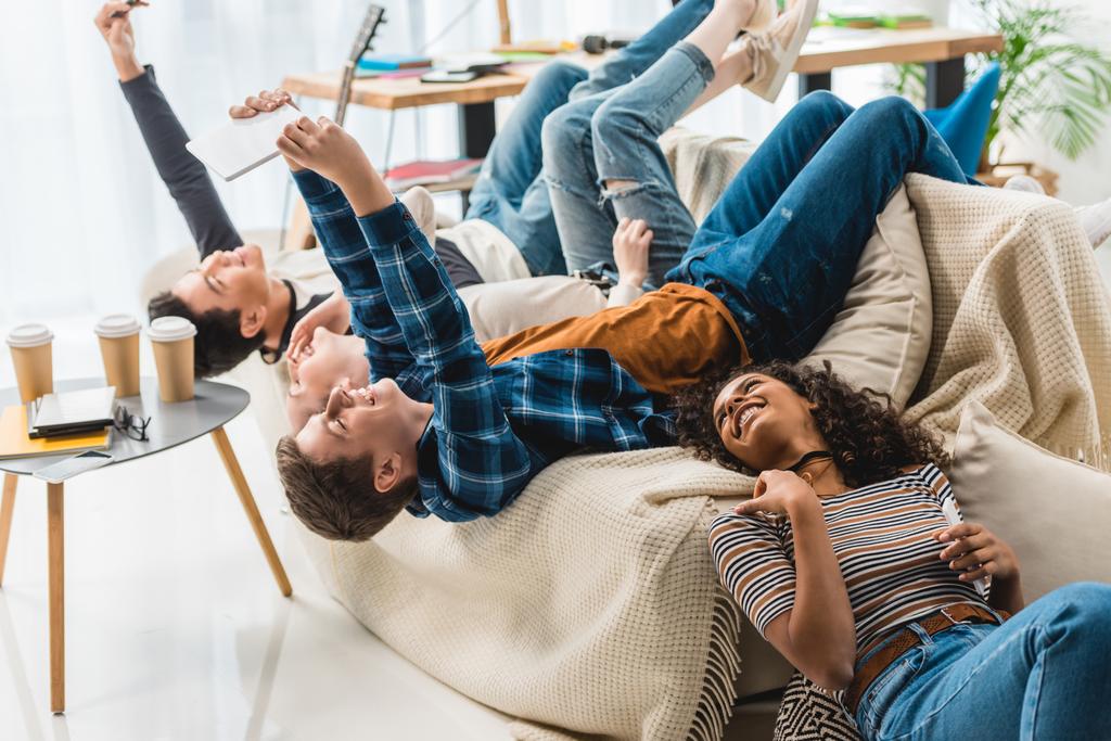 adolescentes deitados no sofá e tomando selfie com tablet e smartphone
 - Foto, Imagem
