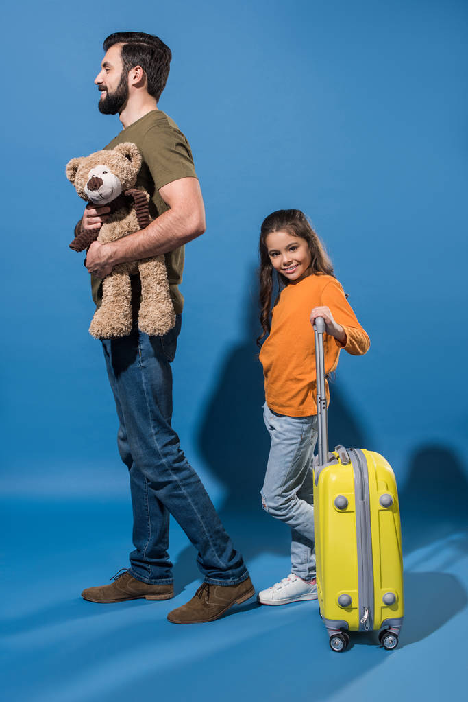 père avec ours en peluche et fille avec sac sur roues sur bleu
 - Photo, image