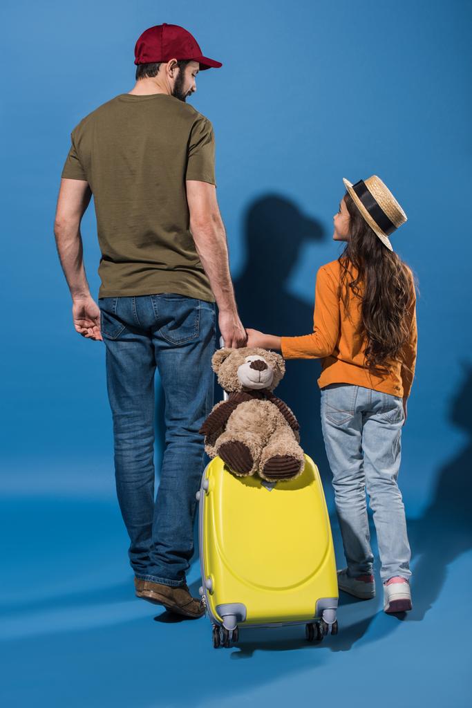 vista trasera de la hija y el padre va con la bolsa de viaje y se mira el uno al otro en azul
 - Foto, Imagen