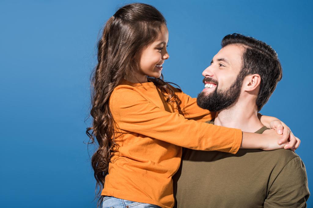 schöner Vater hält Tochter und sie schauen einander auf blau an - Foto, Bild