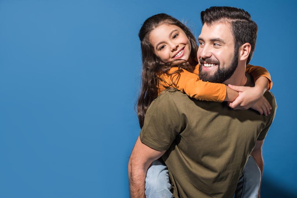 father giving piggyback to smiling daughter on blue - Photo, Image