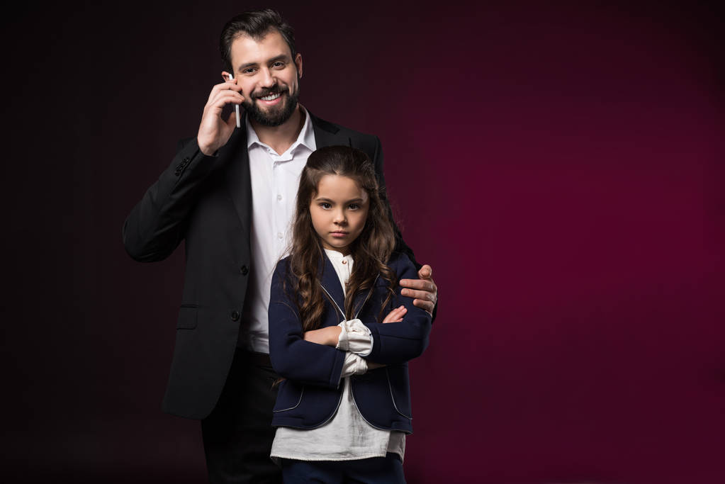 padre che parla con lo smartphone e abbraccia la figlia seria con le mani incrociate sul bordeaux
 - Foto, immagini