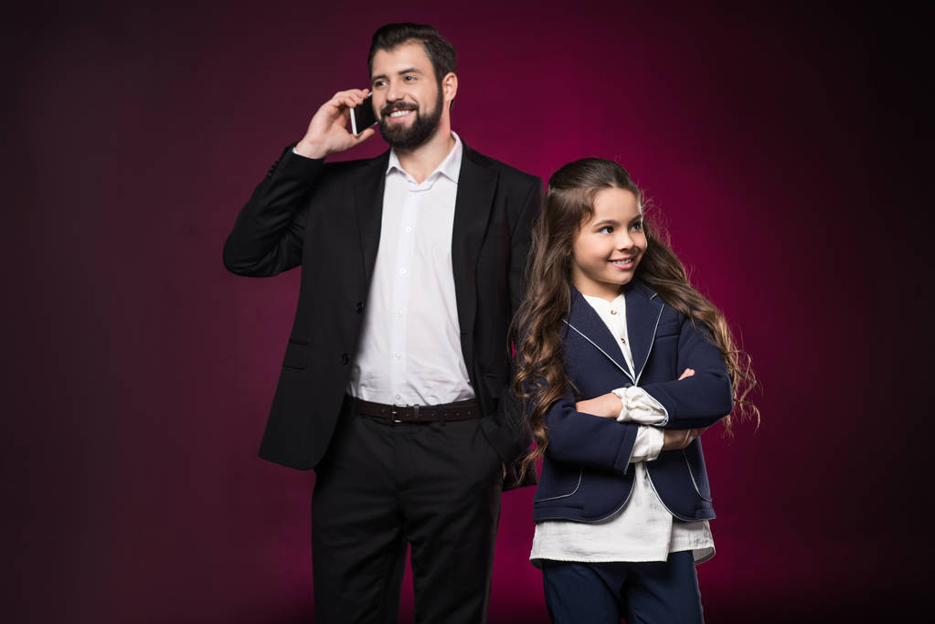 isä puhuu älypuhelimella ja tytär seisoo ristissä kädet viininpunainen
 - Valokuva, kuva