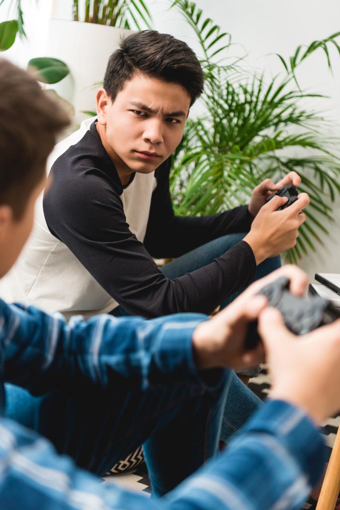 cropped image of angry teen boys looking at each other while playing video game - Photo, Image