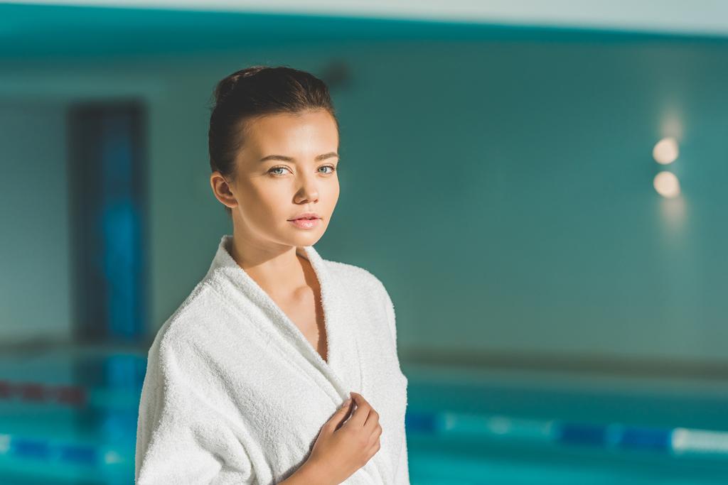beautiful young woman in bathrobe in front of swimming pool at spa - Photo, Image