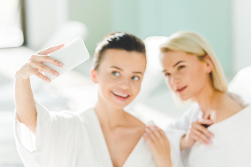 Glückliche junge Frauen in Bademänteln machen Selfie im Wellness-Center - Foto, Bild