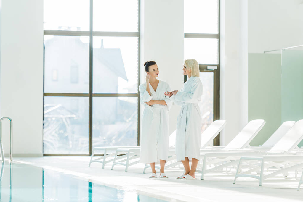 mooie jonge vrouwen in badjassen praten op spa centrum - Foto, afbeelding