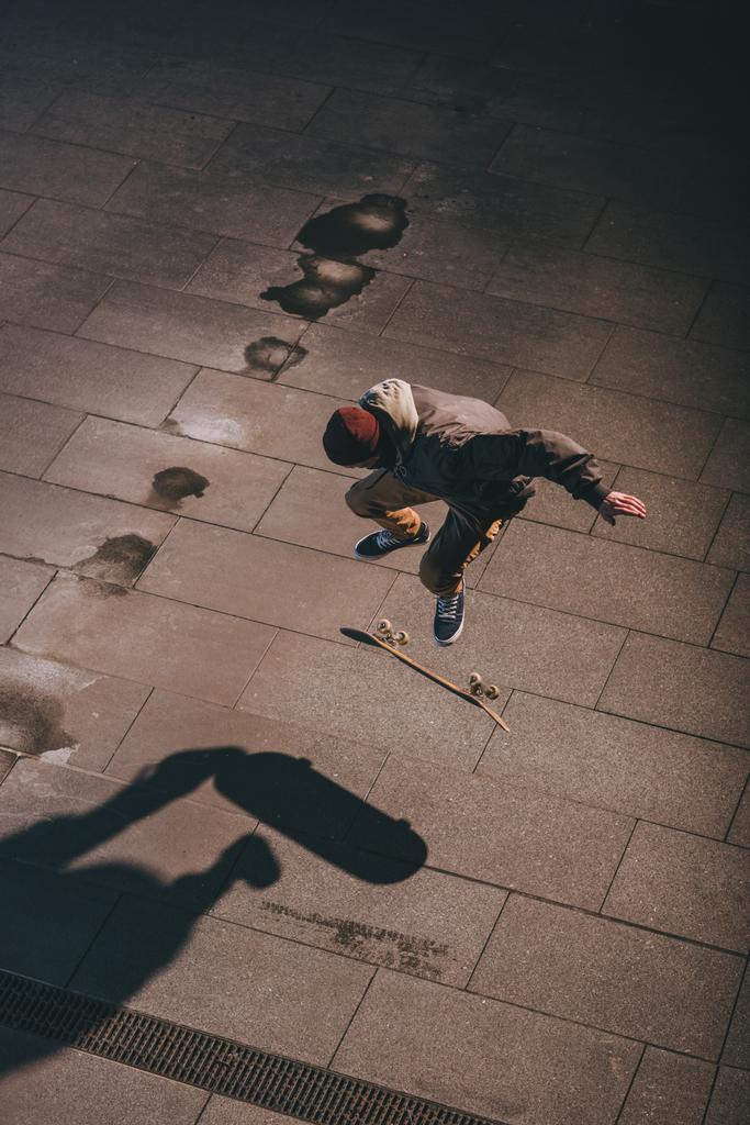 Hochwinkelaufnahme eines Skateboarders, der zu später Stunde einen Sprungtrick im Freien durchführt - Foto, Bild