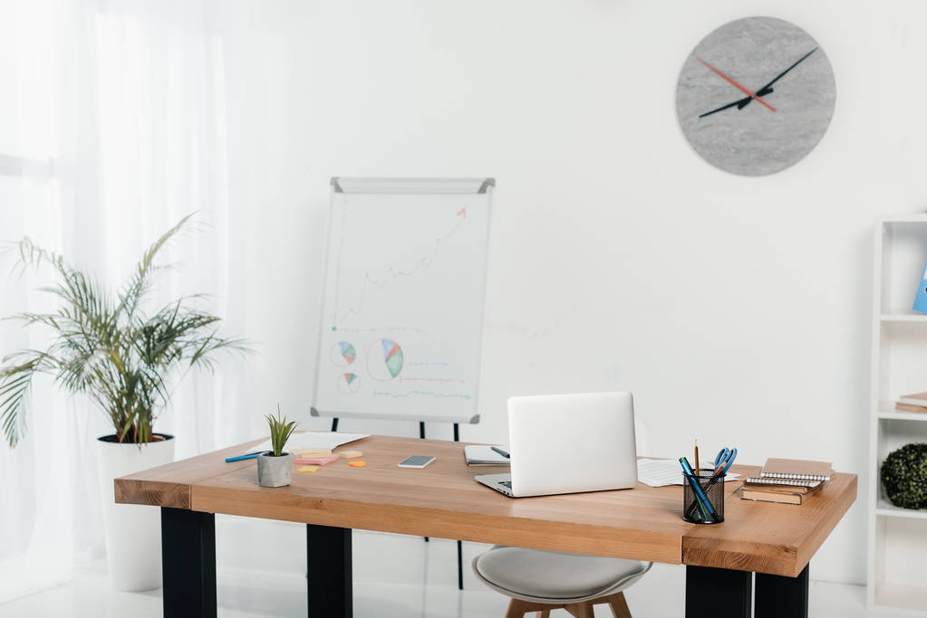werkplek met laptop en office supplies op kantoor met white-board en klok - Foto, afbeelding