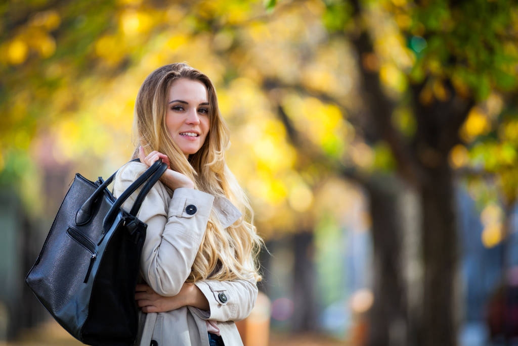 Молодая женщина в пальто улыбается в красочном осеннем городе
 - Фото, изображение