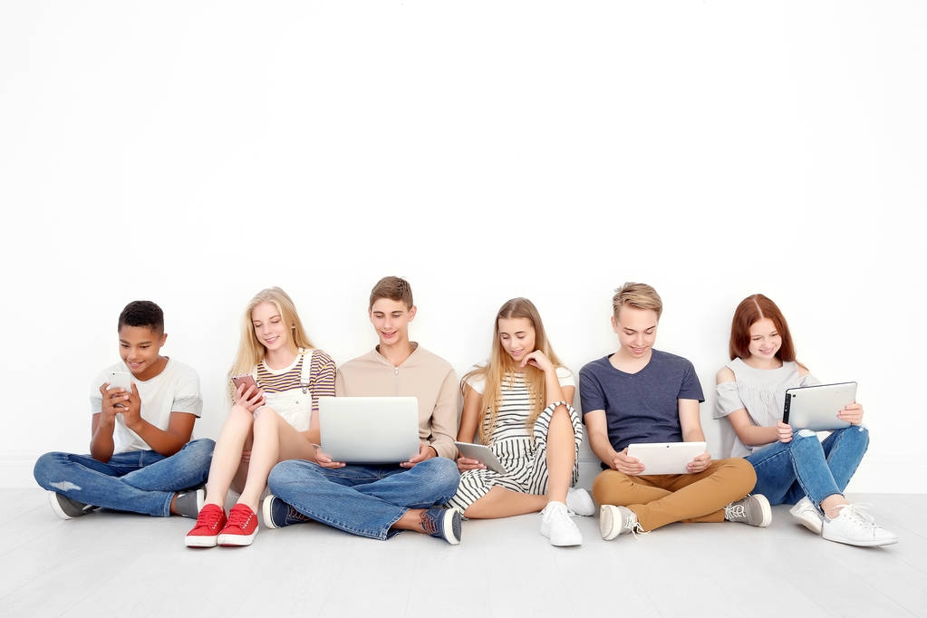 Jugendliche mit modernen Geräten sitzen auf dem Boden in der Nähe einer Lichtwand - Foto, Bild