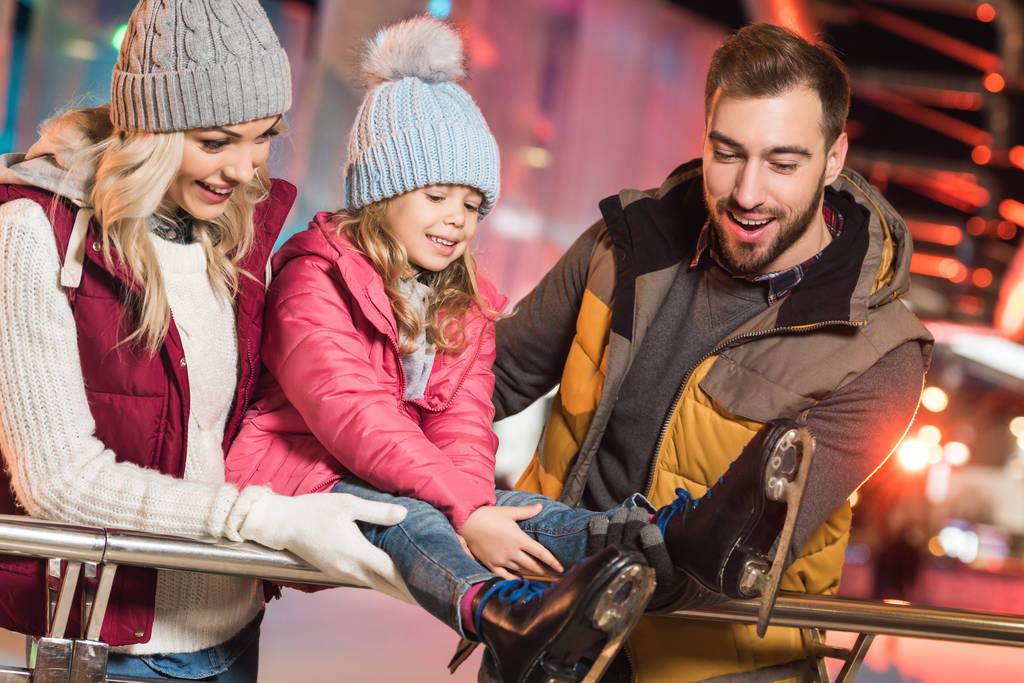 Glückliche Eltern blicken auf süße kleine Tochter mit Schlittschuhen auf Eisbahn  - Foto, Bild