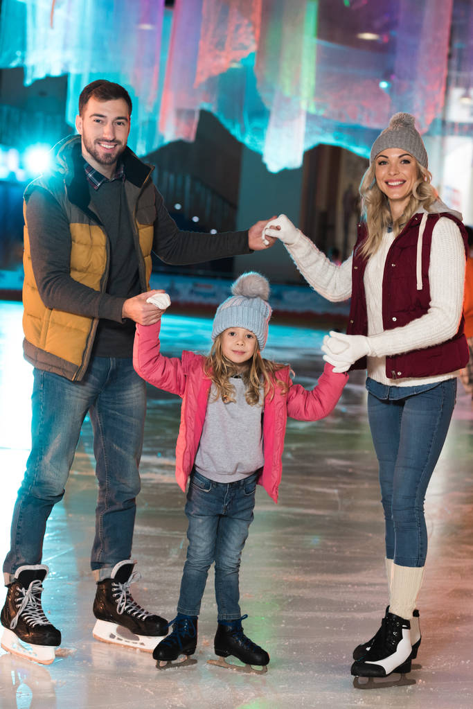 gelukkige jonge familie hand in hand en glimlachend in de camera op de ijsbaan - Foto, afbeelding
