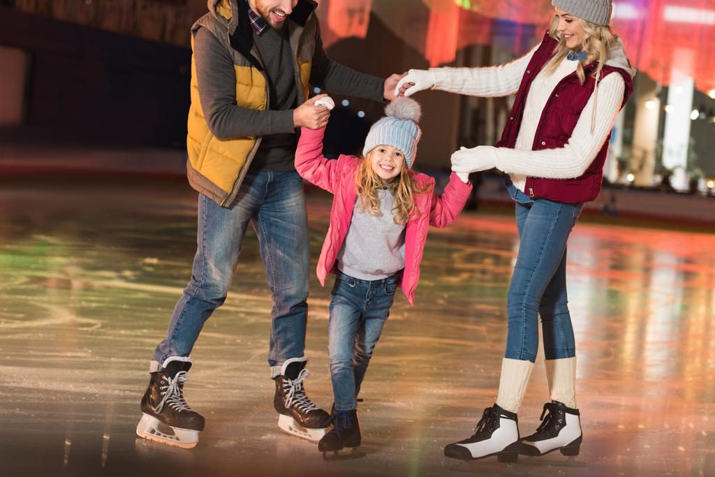 スケート場でスケートを愛らしい小さな娘を教えて幸せな親のショットをトリミング  - 写真・画像