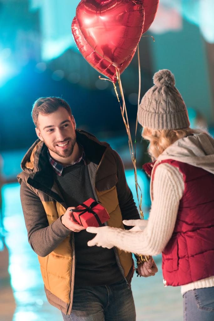 boldog fiatalember barátnője bemutató díszdobozban: Szent Valentin-nap a jégpálya  - Fotó, kép