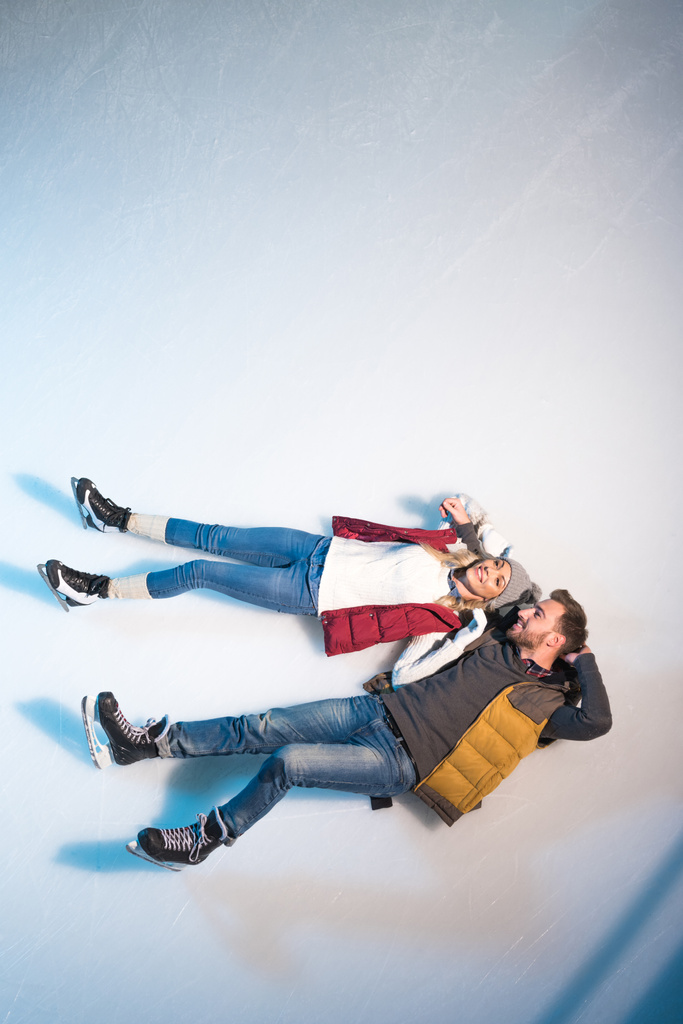 top view of beautiful happy young couple lying together on ice of skating rink - Photo, Image