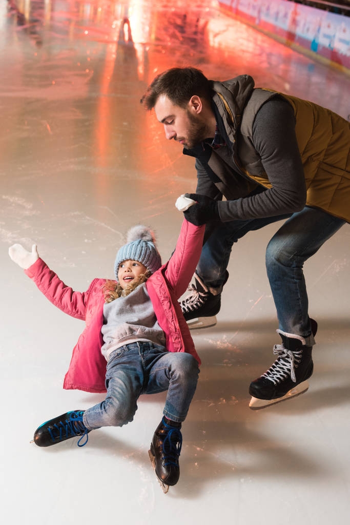 スケート リンクの上に落ちてかわいい小さな娘の手を握っての父 - 写真・画像