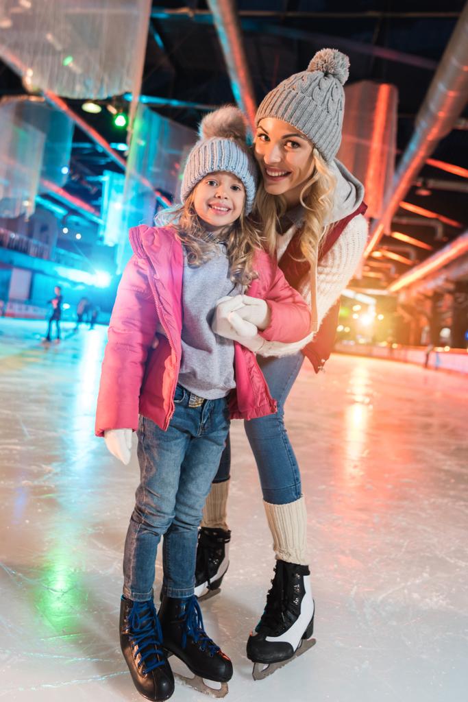 美しい母と娘一緒にスケート リンクに立っている間カメラに笑顔 - 写真・画像