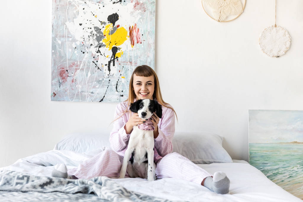 šťastná žena v pyžamu a roztomilé štěňátko odpočívá na lůžku v ráno doma - Fotografie, Obrázek