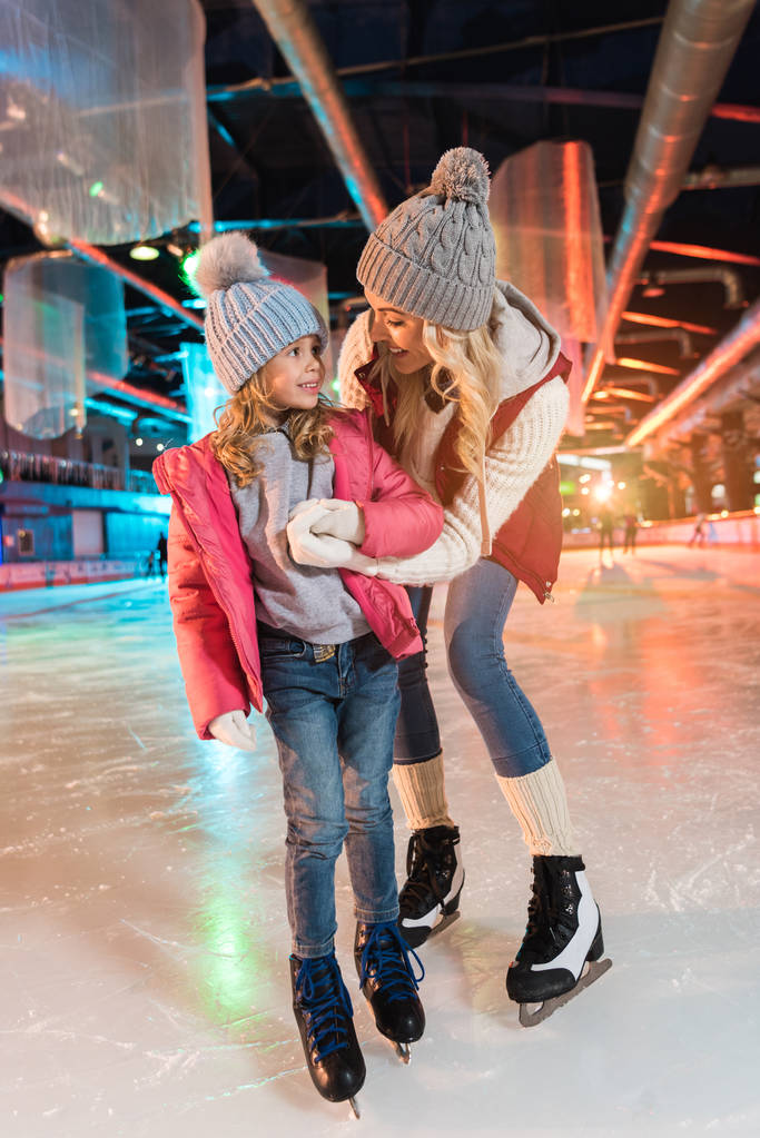 feliz mãe e filha de mãos dadas e sorrindo uns aos outros na pista de patinação
 - Foto, Imagem